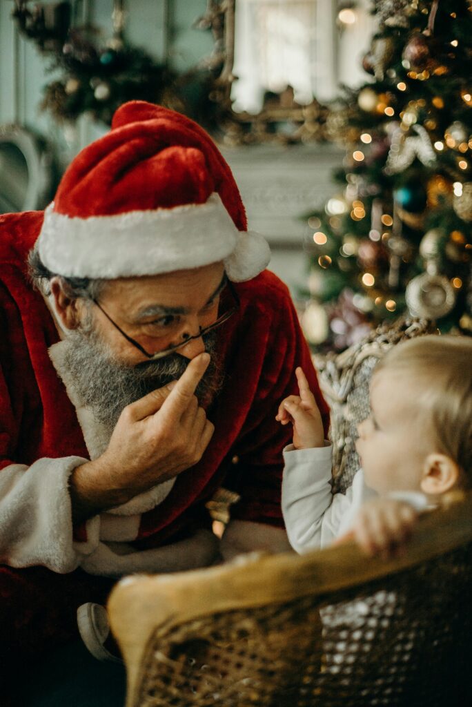 Älterer Mann im Weihnachtskostüm spricht mit einem Kleinkind vor einem geschmückten Weihnachtsbaum – Symbolbild für Weihnachten im DaF-Konversationsmaterial